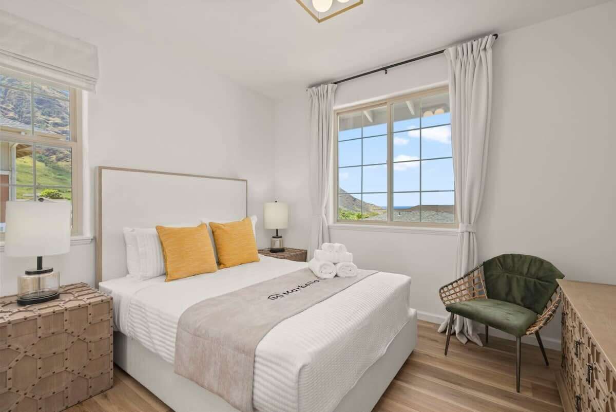 A hotel room with a large bed, a green chair, a nightstand, and a window with curtains.