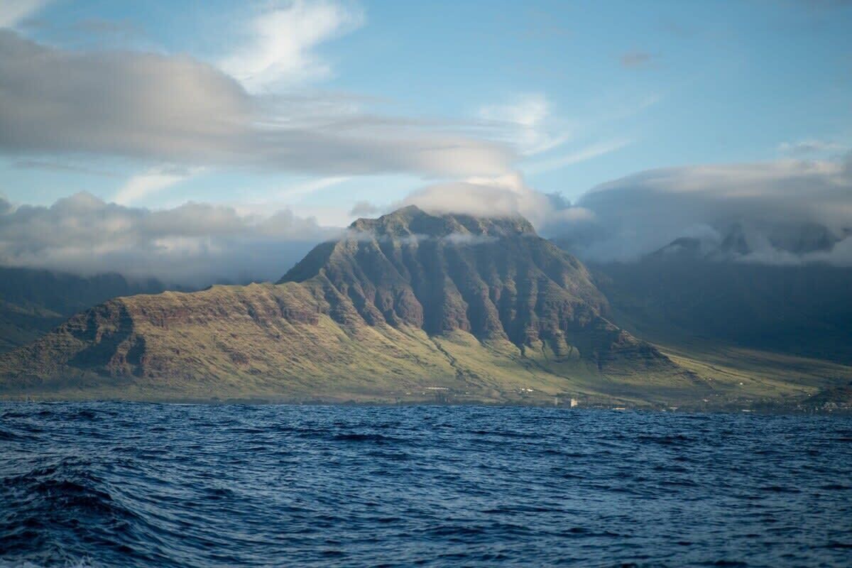 A mountain with a rugged peak, surrounded by clouds and overlooking a body of water.