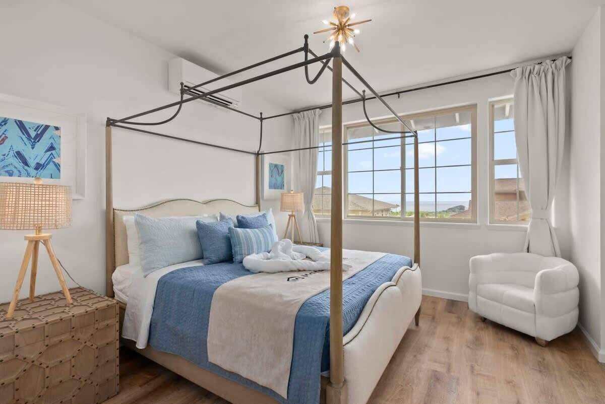Una cama con dosel con vista al mar, un sillón blanco y una mesita de noche con diseño geométrico.