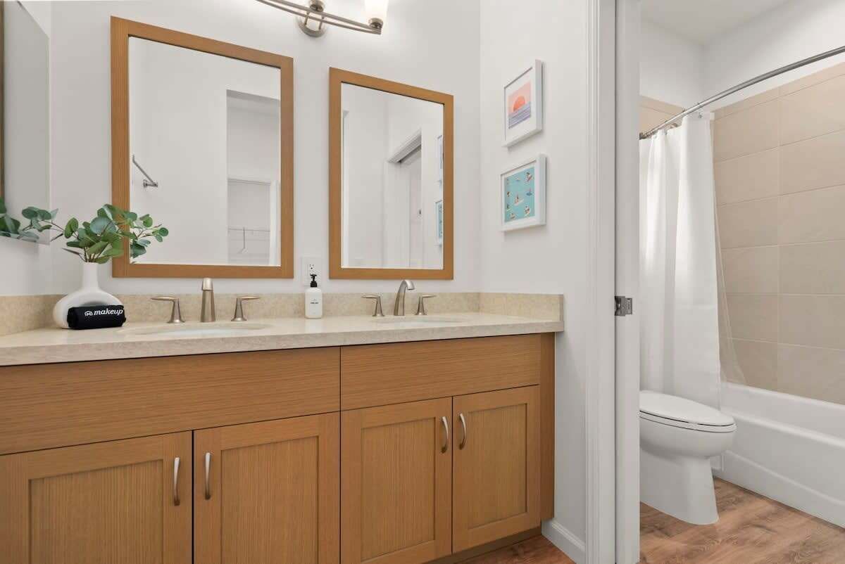 A bathroom with a wooden vanity, two mirrors, a sink, and a shower area.