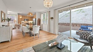 A modern interior with a dining area, kitchen, and a large sliding glass door leading to an outdoor patio. - @marbella Lane - Paradise Gem W/breathtaking Views (Waianae)
