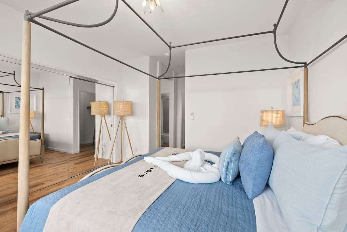 A modern hotel room with a four-poster bed, a large window, and a view of the hallway.