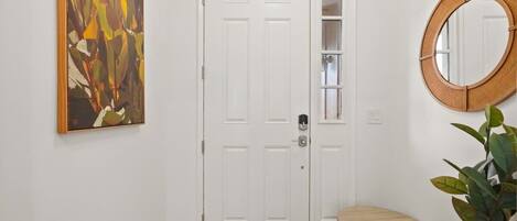 A hallway with a white door, a round mirror, and a wooden bench.
