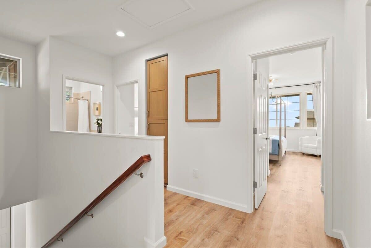 Un interior moderno con una escalera de madera, un pasillo que lleva a un dormitorio y un baño con ducha y retrete a la vista.