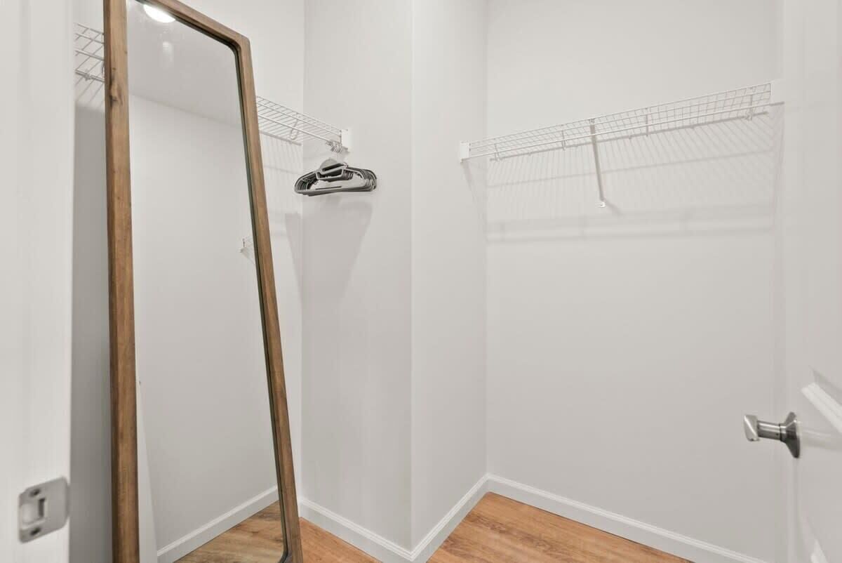 A room with white walls, a wooden floor, a large mirror, and a metal rack.