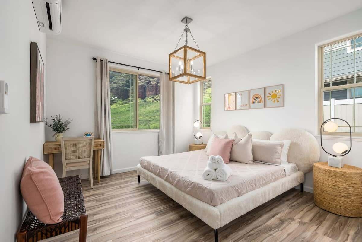 A bedroom with a large bed, a desk, a chair, and a view of greenery outside.