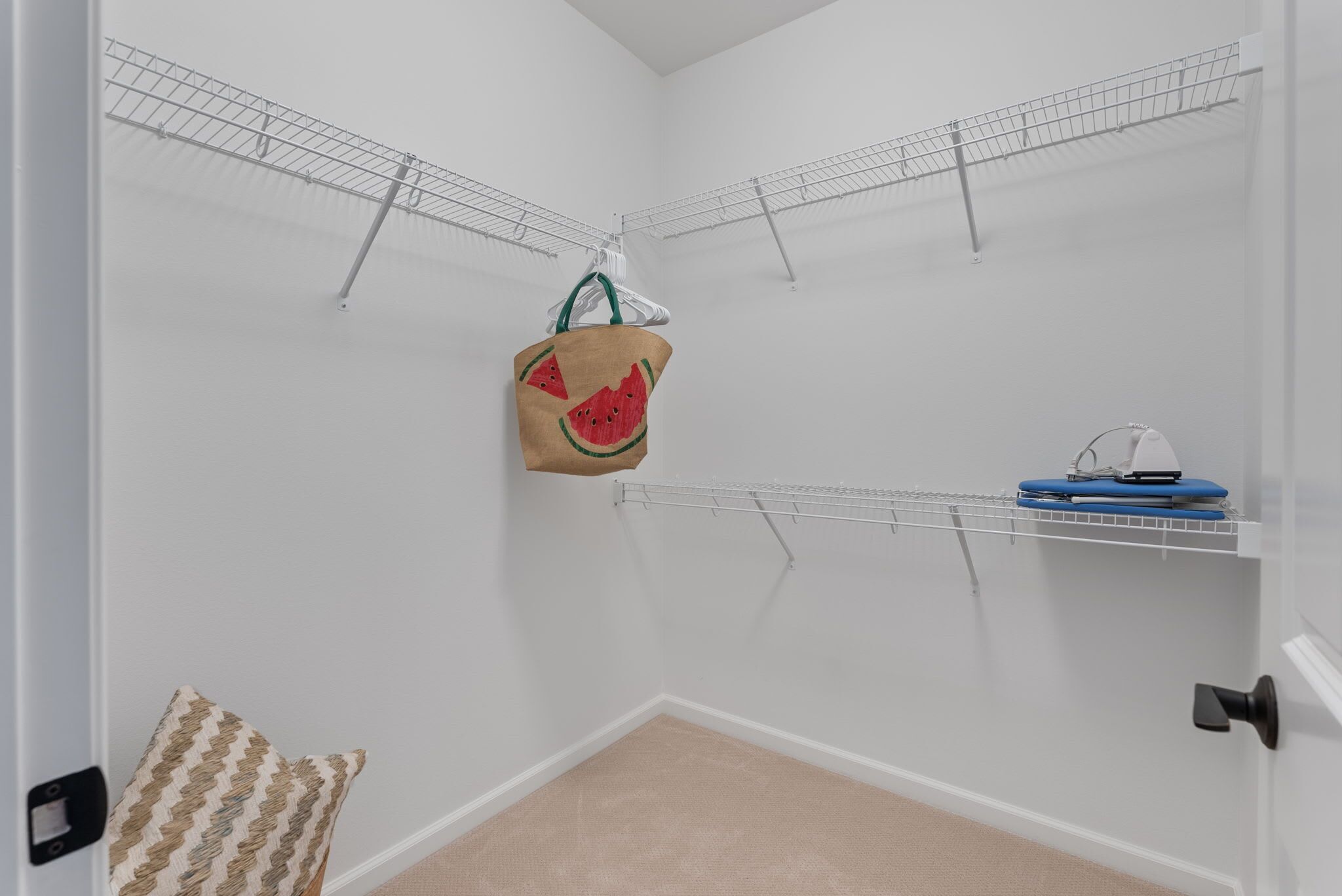 A laundry room with metal drying racks, a blue ironing board, and a brown tote bag with watermelon designs.