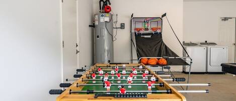 A room with a foosball table, a water heater, and a basketball hoop.