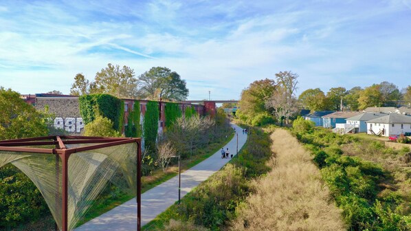 Ein Weglauf entlang eines Flusses mit einer Brücke im Hintergrund, umgeben von Grünflächen und Wohnhäusern.