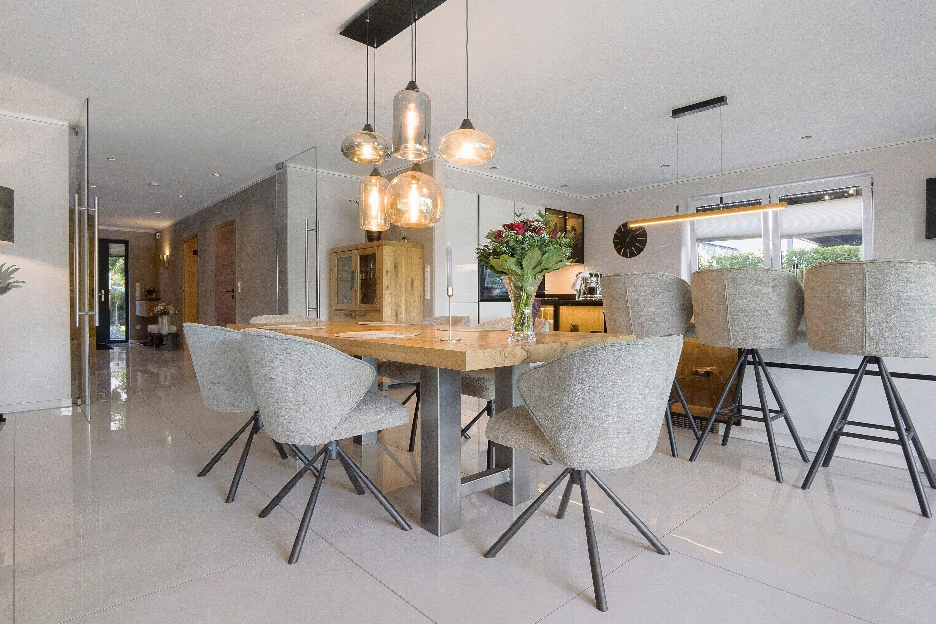 Un espace de salle à manger moderne avec une table centrale, des chaises à revêtement gris et des luminaires suspendus.