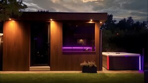 A modern building with a wooden exterior, a glass door, and a hot tub with LED lighting. - Luxurious 'Schaffner' Apartment with Private Pool, Sauna, Hot Tub, Terrace & Wi-Fi (Warendorf)