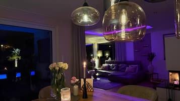 Ein modernes Wohnzimmer mit einem Holzesstisch, einer Couch und Pendelleuchten.