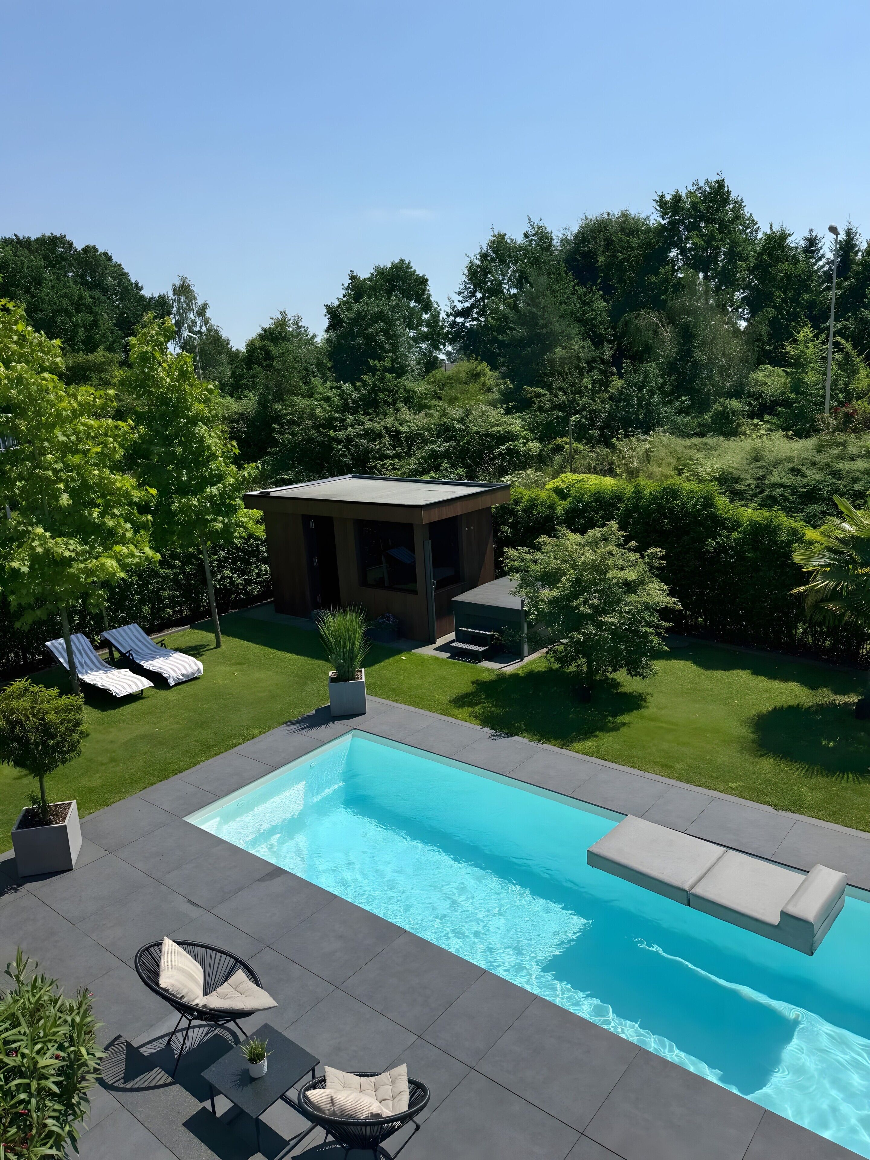 Une piscine avec des chaises longues, un petit bâtiment et de la verdure environnante.