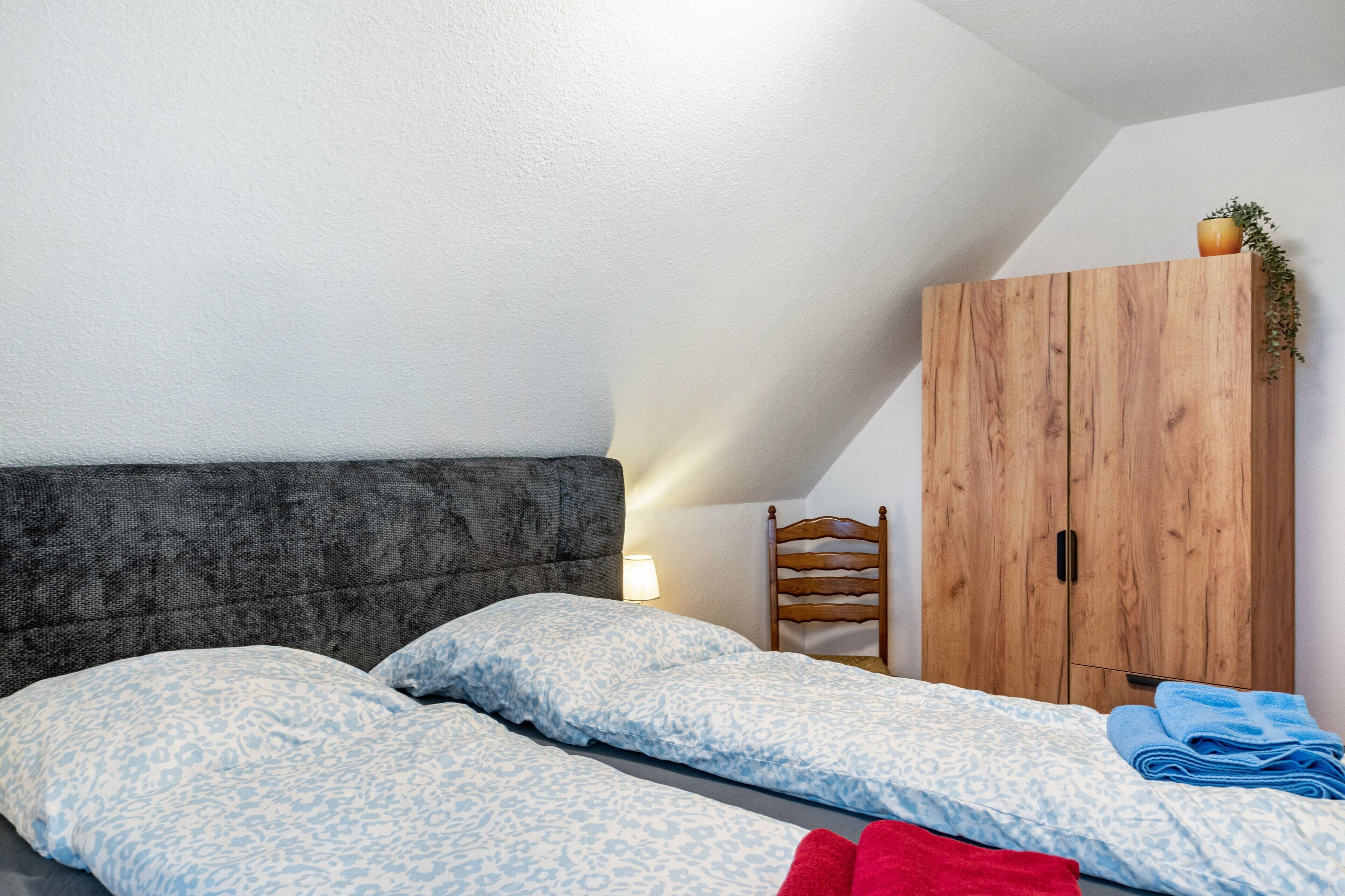 Een slaapkamer met een bed, een houten garderobe en een kleine stoel.