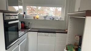 Une cuisine compacte avec des meubles blancs, un four encastré, un lave-vaisselle et une fenêtre au-dessus de l’évier.