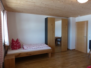 Ein Zimmer mit Holzboden, einem Bett mit floralem Überwurf, einem Stuhl und einem Kleiderschrank.