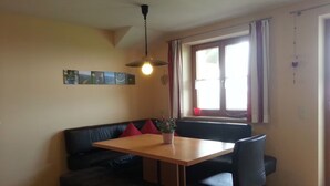 A dining area with a wooden table, black leather sofa, and a hanging light fixture.