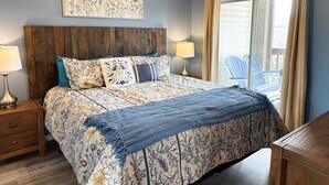 Une chambre à coucher avec une tête de lit en bois, une couvre-lit à motifs floraux, deux lampes de chevet, un ventilateur de plafond et une grande fenêtre avec des rideaux.