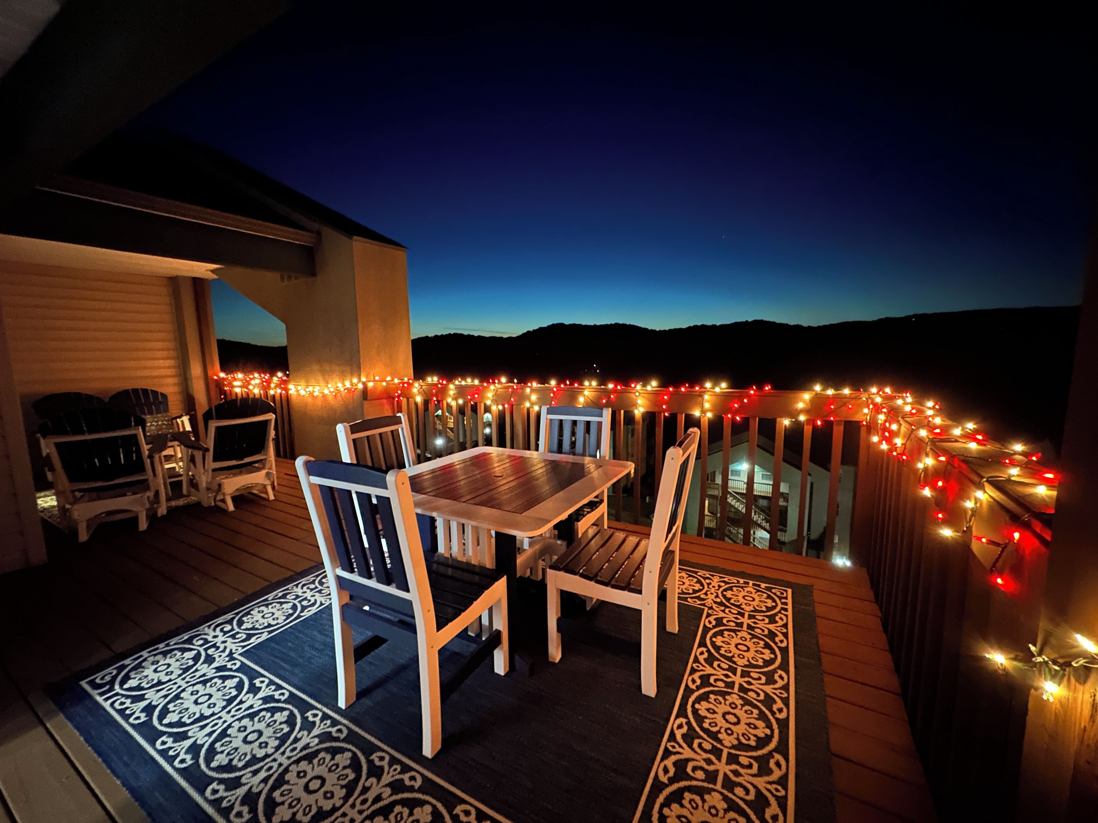 An outdoor deck with a table and chairs, surrounded by string lights.