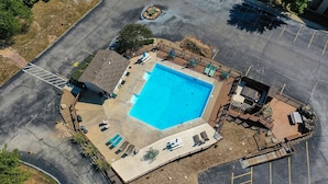Vue aérienne d’un espace piscine comprenant une terrasse, des chaises longues et un coin barbecue.