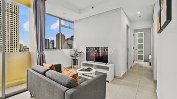 A modern living room with a grey sofa, a flat-screen TV, and a city view through large windows.