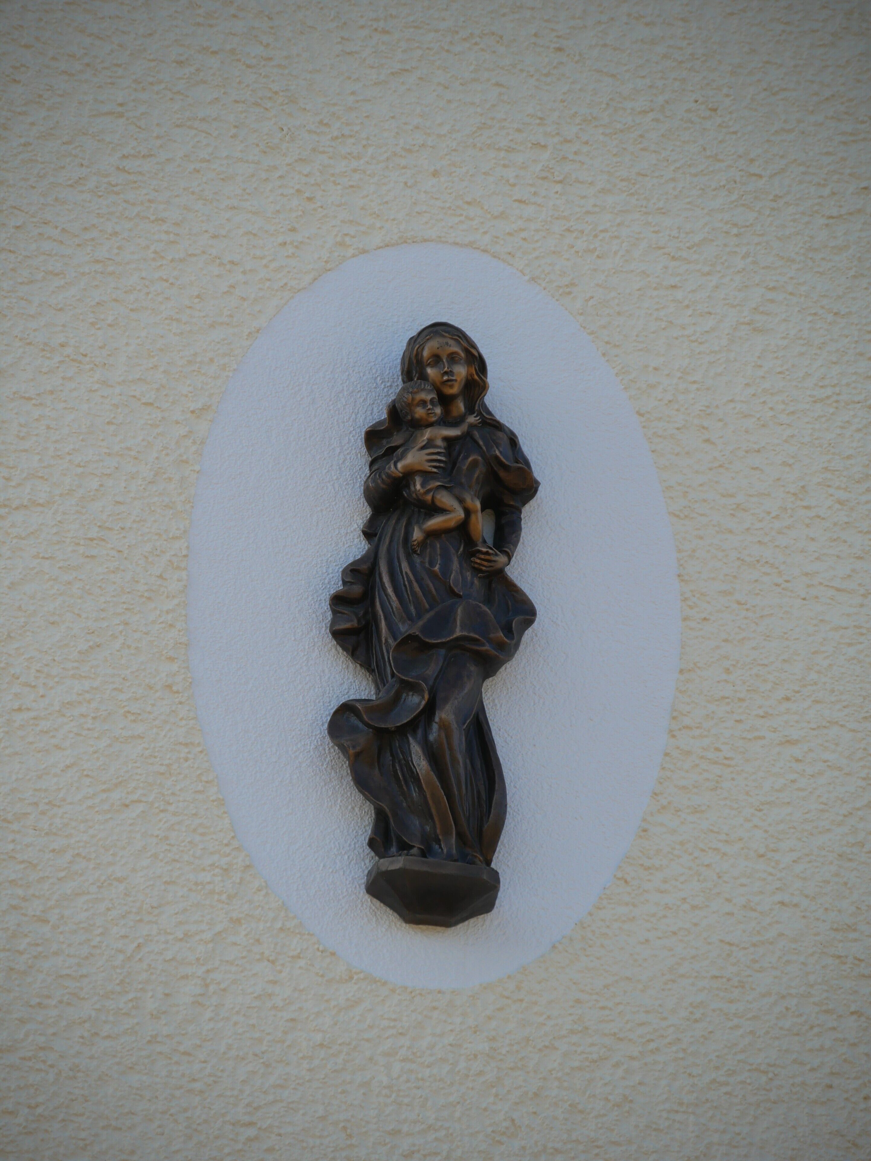 A wall-mounted sculpture of a figure holding a child, with a textured wall background.