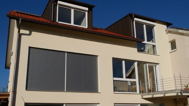 A multi-story building with large windows, a balcony, and a visible garage door. - Single Room with Wi-Fi (Wäschenbeuren)