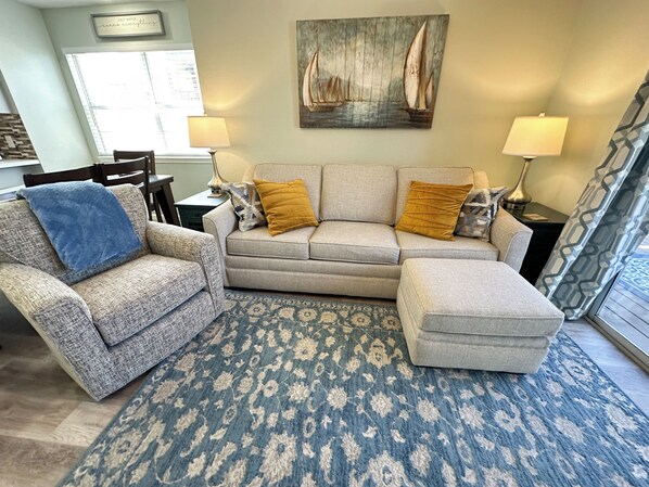 A living room with a sofa, armchair, patterned rug, and a painting on the wall.