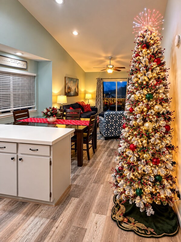 A dining area with a Christmas tree, a ceiling fan, and a window with curtains.