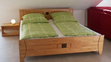 Un lit en bois avec une tête de lit, deux oreillers, une table de chevet avec une lampe, et un canapé rouge en arrière-plan.