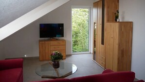 A modern living room with a TV, a glass coffee table, red sofas, and a wooden cabinet.