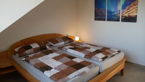 A bedroom with a bed, pillows, a bedside lamp, and three wall-mounted pictures.