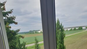 Un balcón con mesa y sillas, vistas a un campo verde y un edificio en la distancia.