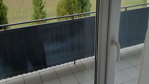 Un balcón con vistas a un campo verde y árboles, suelo de baldosas y una puerta con manija.