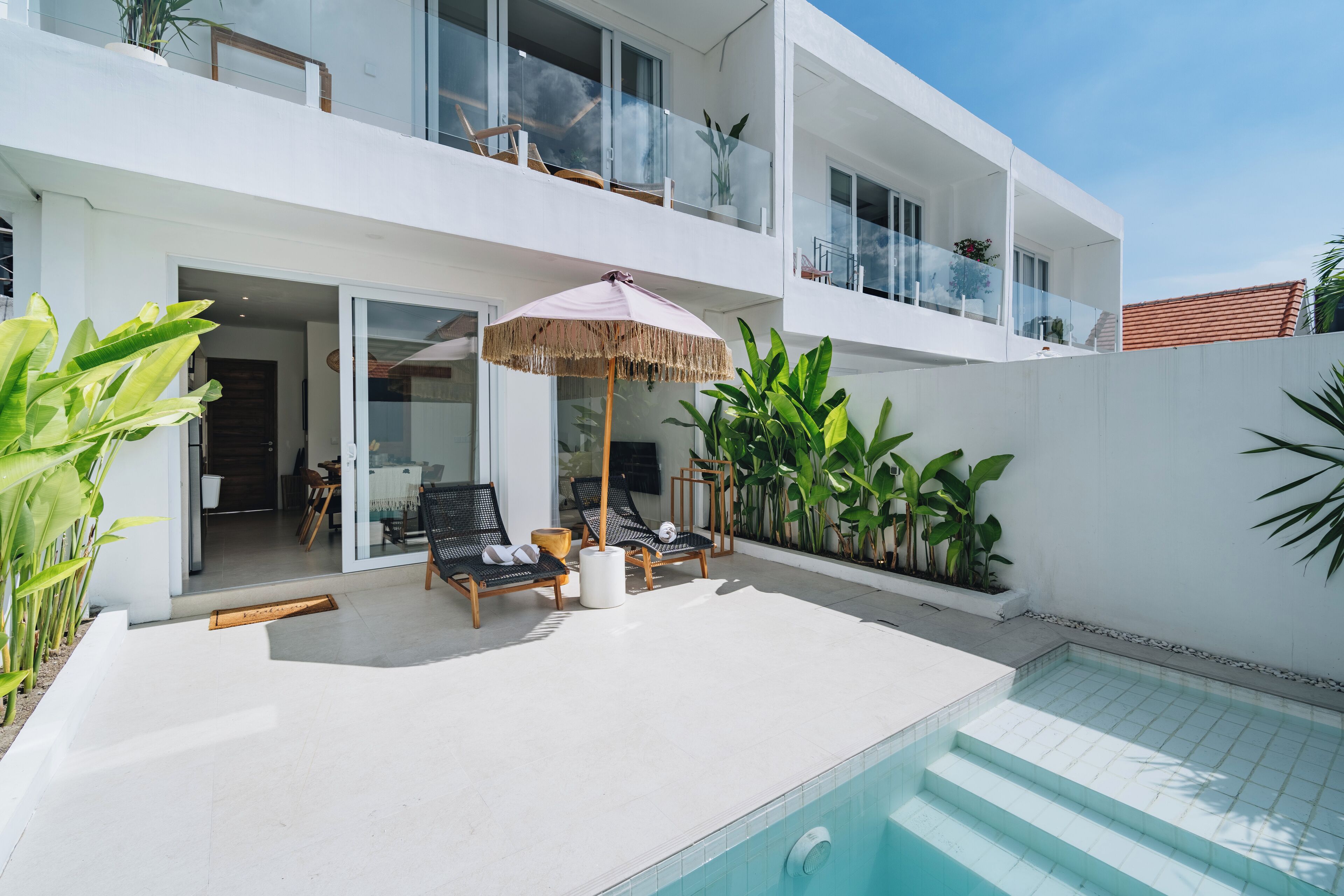Uma casa moderna de dois andares com piscina, área de estar externa e vegetação exuberante.