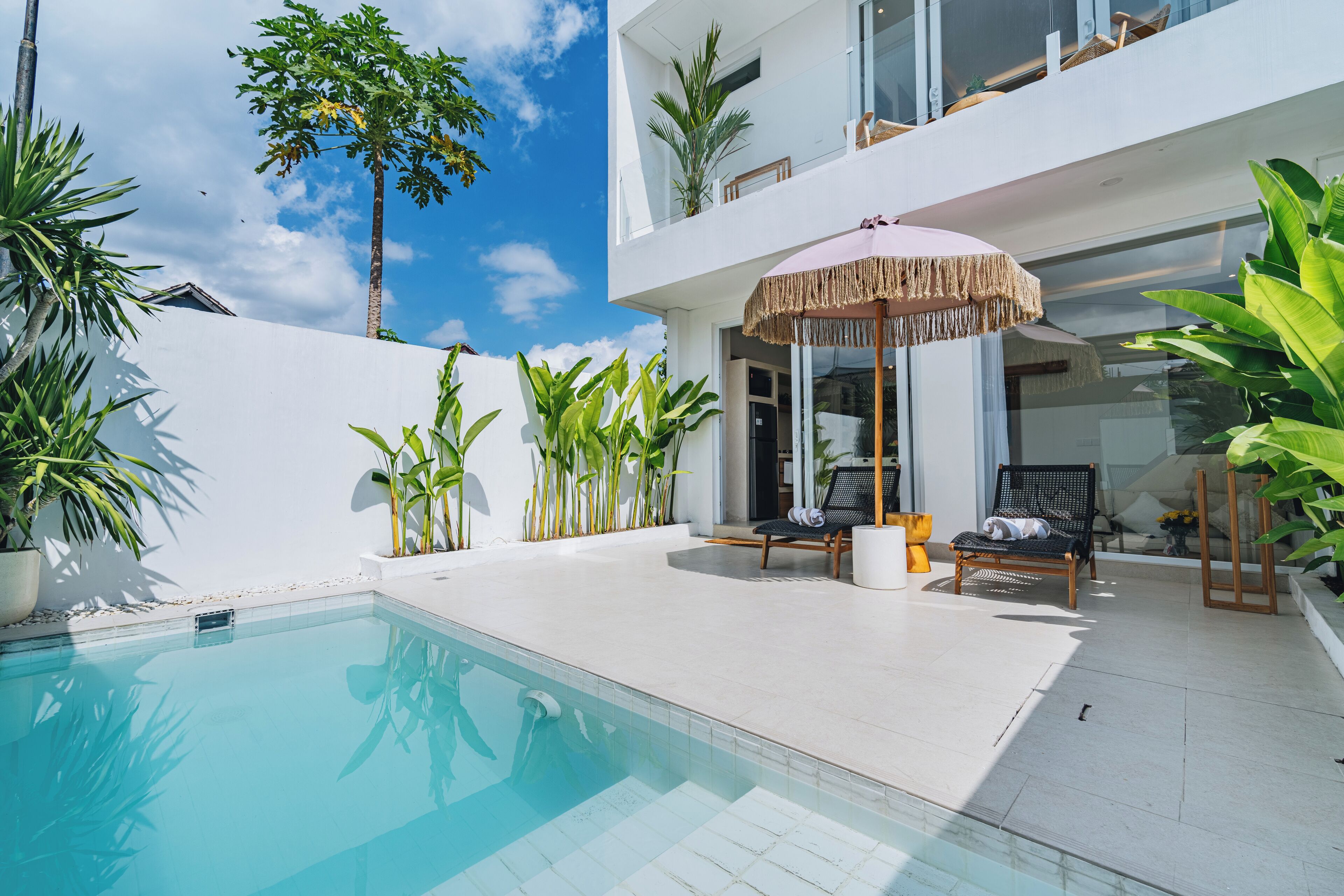 A modern outdoor pool area with a clear blue pool, surrounded by potted plants and lounge chairs.