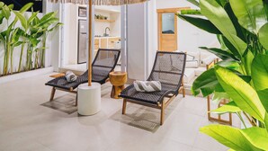 A modern outdoor lounge area with two lounge chairs, a large umbrella, and potted plants. - Villa Balinay (Canggu)