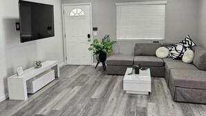 A modern living room with a grey sofa, white coffee table, and a flat-screen TV mounted on the wall.