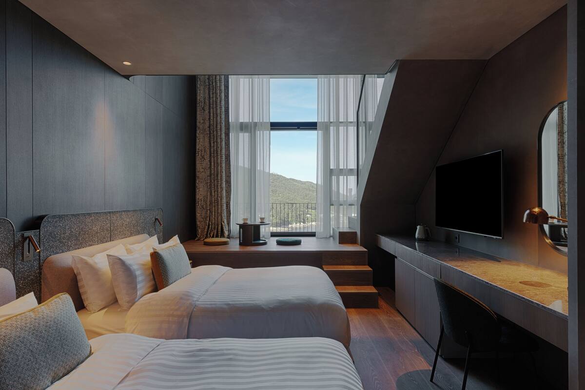 A modern hotel room with a large bed, a desk, a TV, and a view of the outdoors.