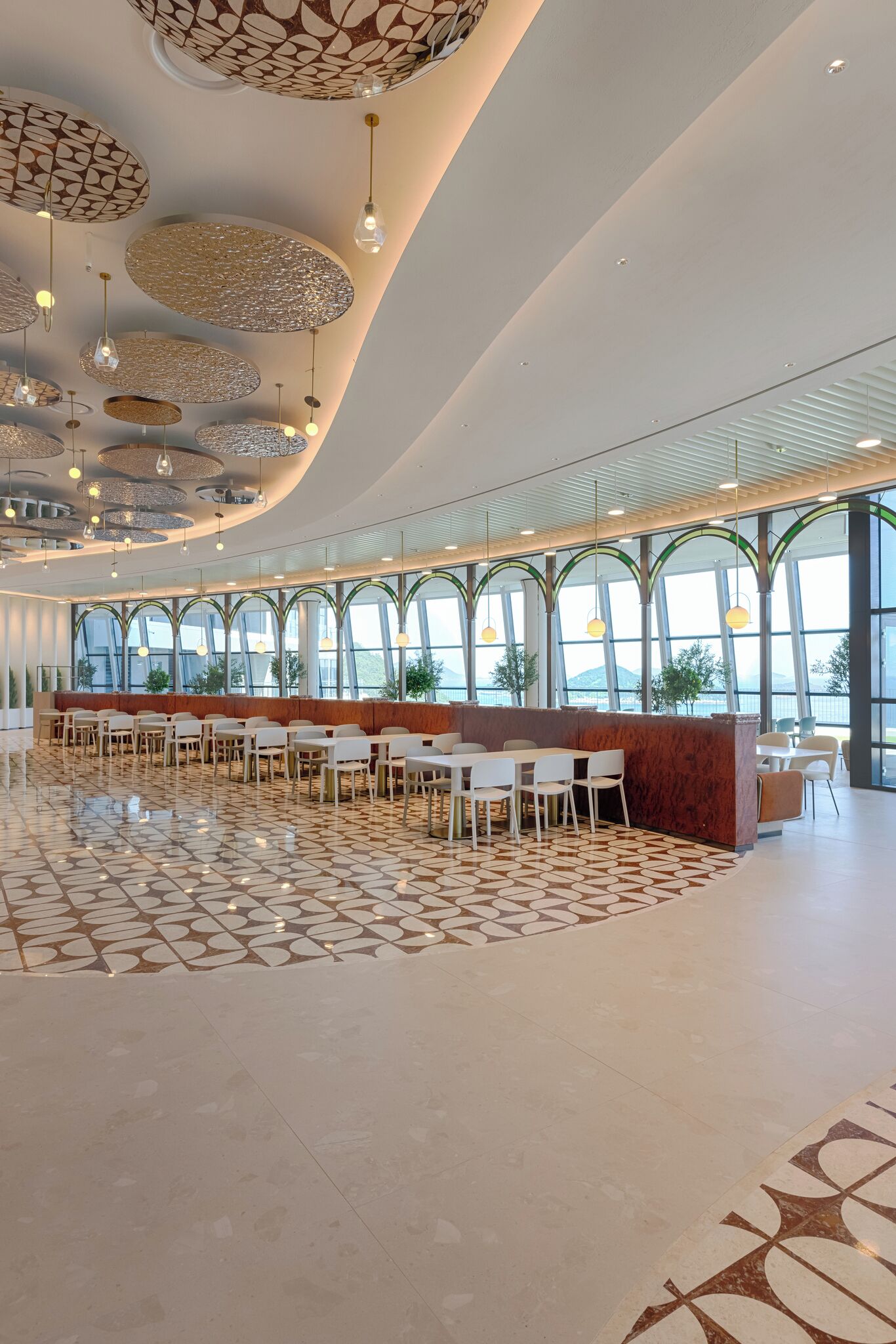 A spacious indoor area with a modern design, featuring a long counter with seating, large windows, and a patterned floor.