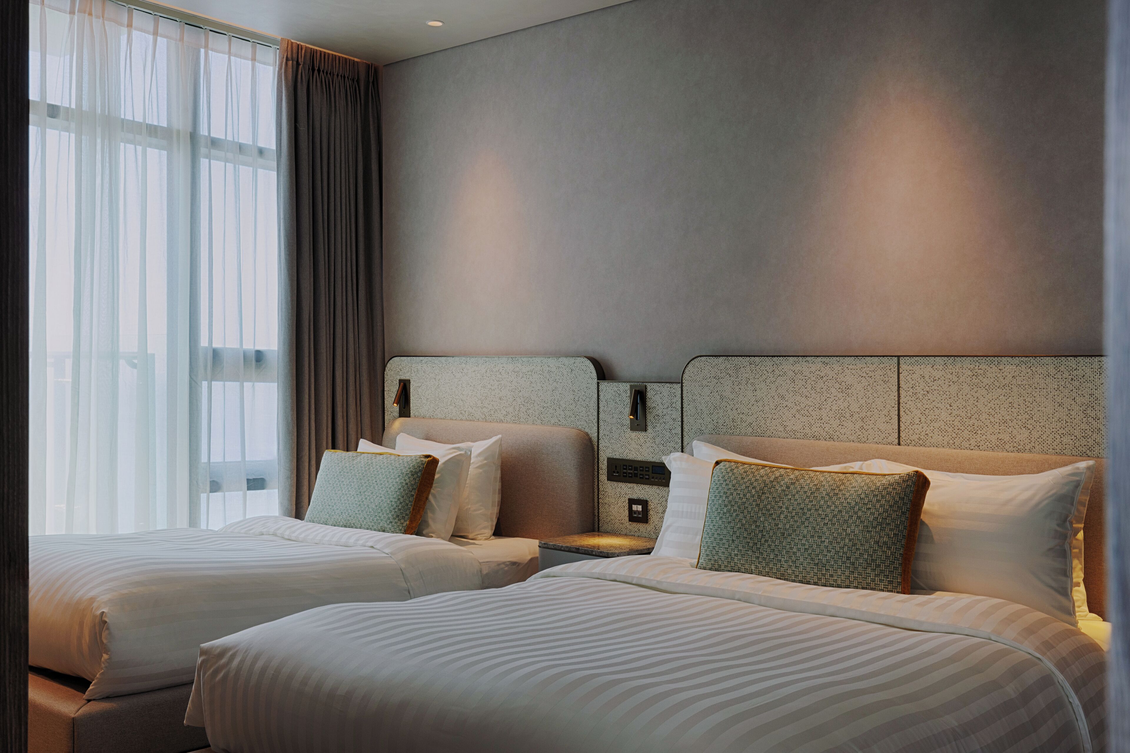 Une chambre d’hôtel avec deux lits, une grande fenêtre avec des rideaux et un mur à motifs.
