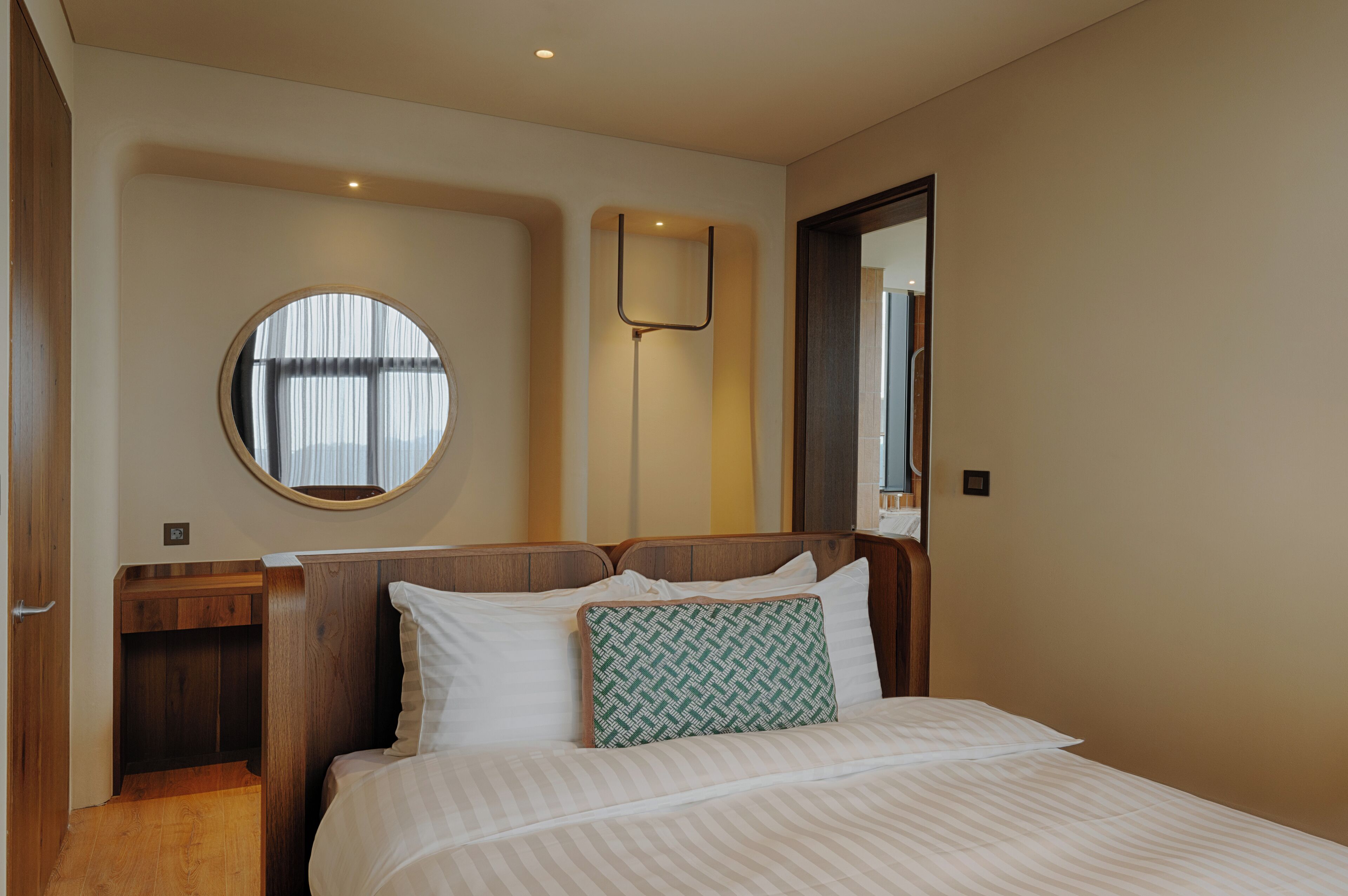 Ein Hotelzimmer mit einem Bett, einem Nachttisch, einem Spiegel und einem runden Fenster.