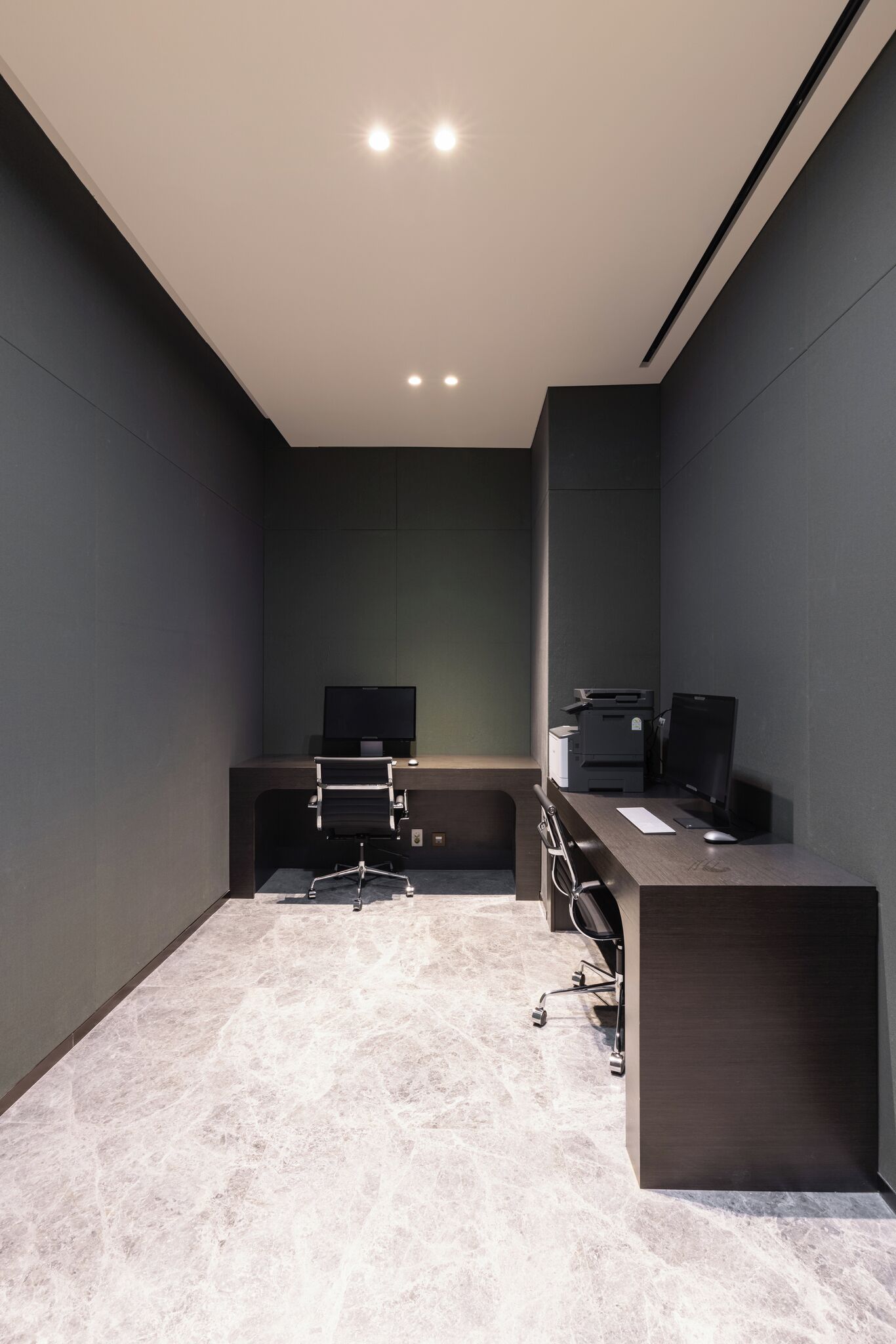 Un espacio de oficina moderno con un escritorio de color oscuro, una silla, un monitor de pantalla plana, una impresora y un ordenador.