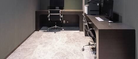 Un espacio de oficina moderno con un escritorio de color oscuro, una silla, un monitor de pantalla plana, una impresora y un ordenador.