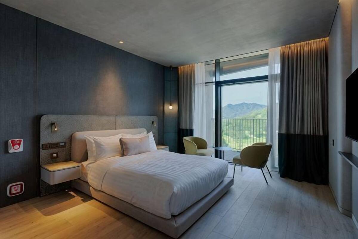 A modern hotel room with a large bed, bedside tables, a TV, and a view of the outdoors.