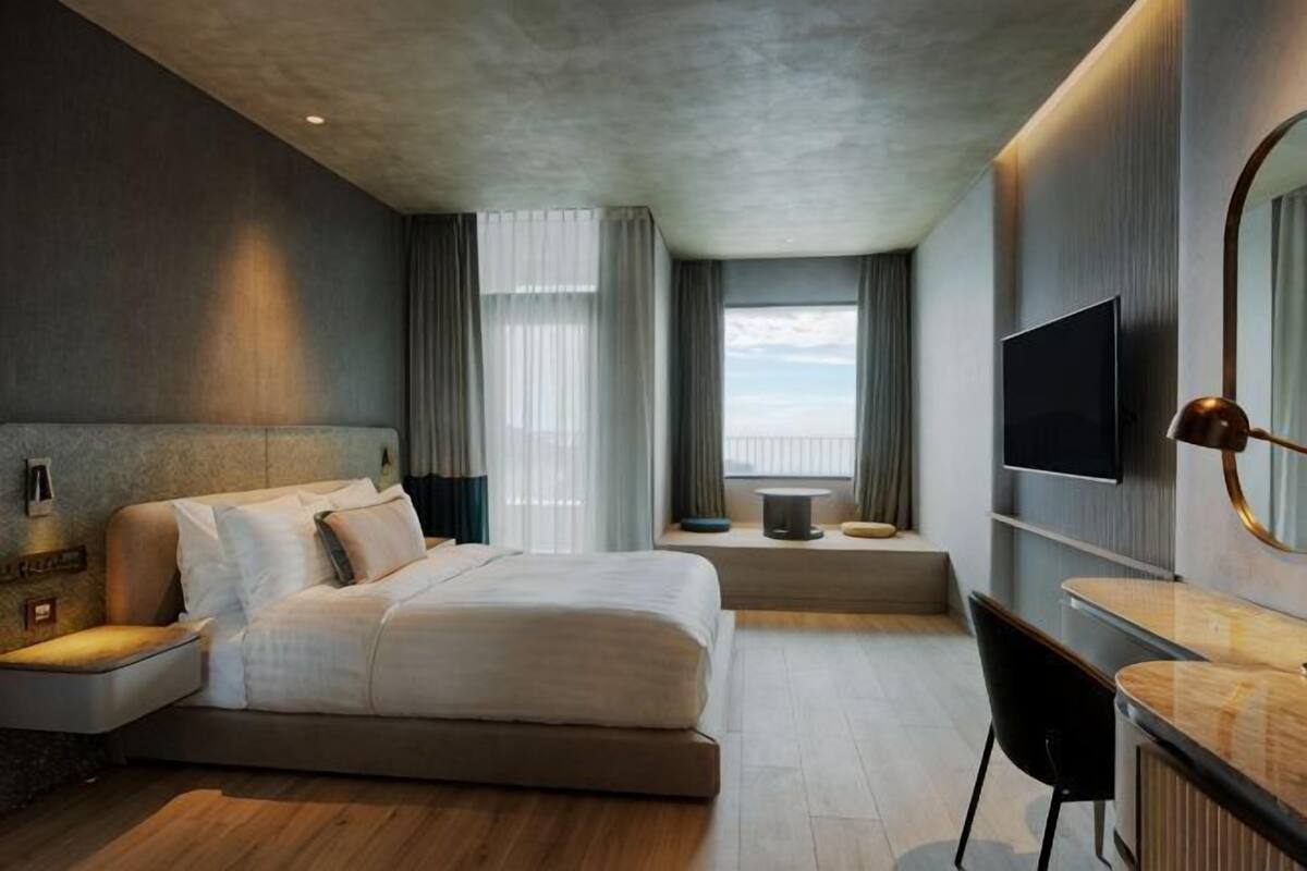 A modern hotel room with a large bed, a desk, a TV, and a view of the outdoors.