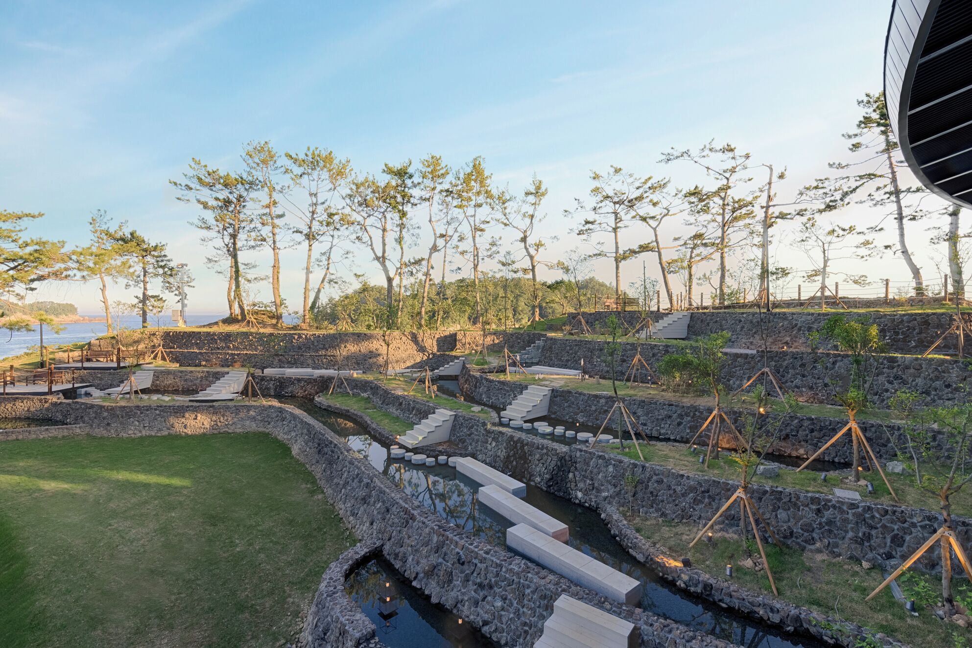 A landscaped garden with stone pathways, a small water feature, and a view of the sea.