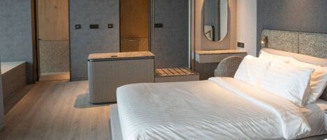 A modern hotel room with a large bed, a small seating area, and a mirror on the wall.