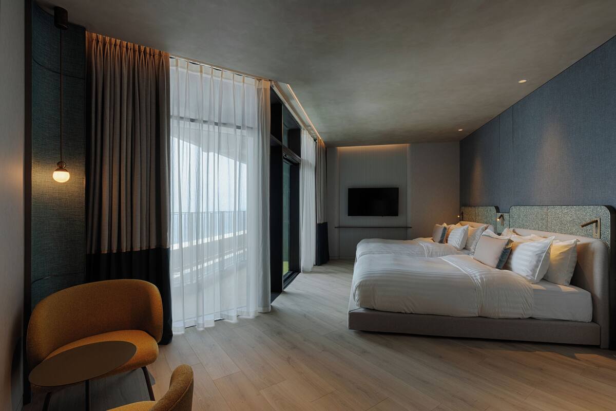 A modern bedroom with a large bed, a TV mounted on the wall, and a seating area with a chair and table.