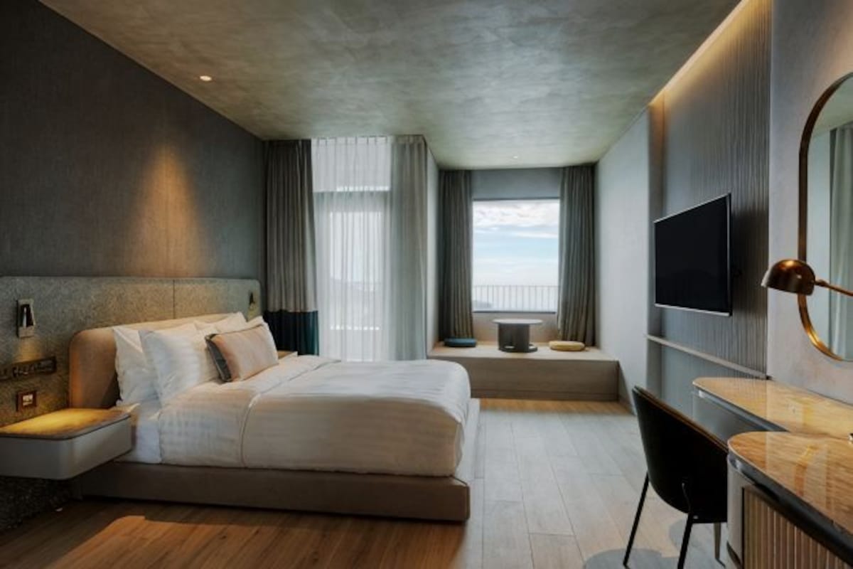 Een moderne hotelkamer met een groot bed, een bureau, een televisie en uitzicht op het omliggende landschap.